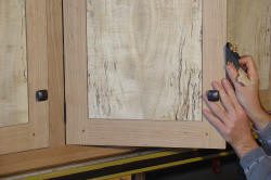 Hands sanding wooden cabinet door edges.