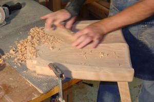 Person shaping wood with hand tool.