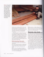 A person crouches near stacked wooden boards in a workshop, holding a measuring tool.