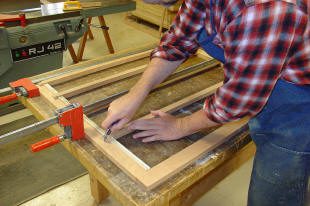 Person measuring wood on workbench with clamps.