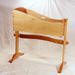 A wooden baby cradle with a curved design, supported by two legs and set against a white background.