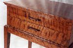 A close-up view of a wooden table with two drawers, featuring a glossy finish and a distinctive wavy grain pattern.