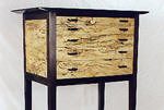 A small wooden cabinet with four drawers and dark legs, featuring light-colored, patterned wood on the drawer fronts and sides.
