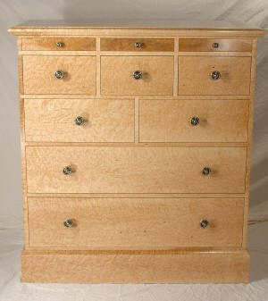 Light wood dresser with nine drawers of varying sizes, each with a round metal knob, set against a plain background.