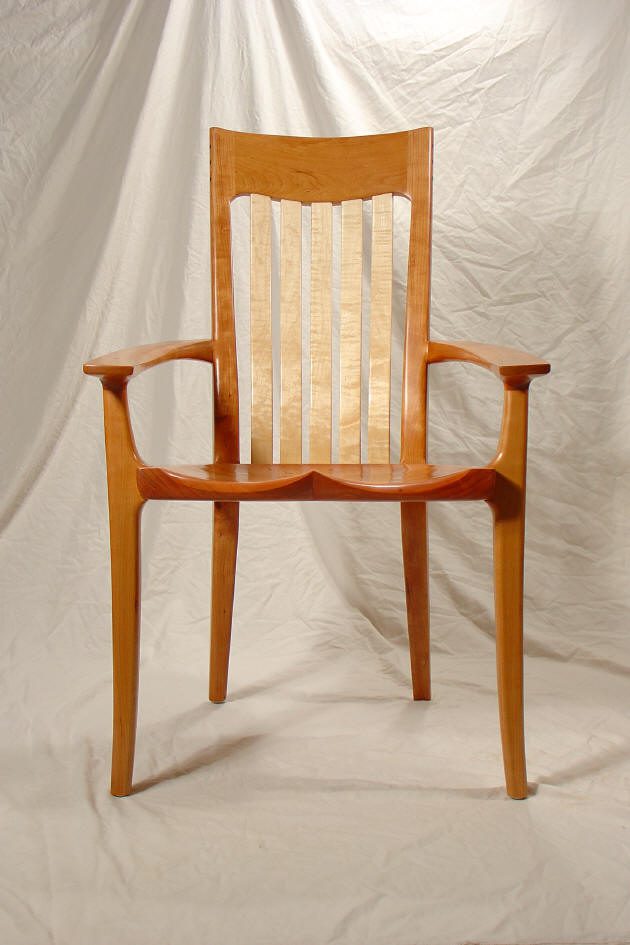 A wooden armchair with a high slatted back, curved armrests, and a contoured seat, set against a draped white fabric background.