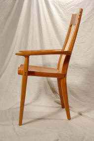 Wooden armchair with a slightly reclined backrest, angled legs, and a simple, modern design, set against a plain, light-colored fabric backdrop.
