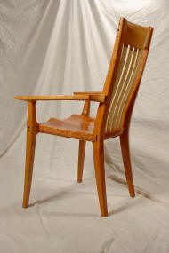 A wooden armchair with a slatted backrest and contoured seat, positioned on a neutral fabric backdrop.