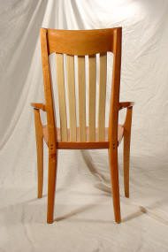 Wooden chair with vertical slats on the backrest, curved arms, and tapered legs, shown against a plain white backdrop.