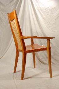 Wooden chair with a high backrest and armrests, featuring a natural wood finish, photographed against a plain white fabric backdrop.