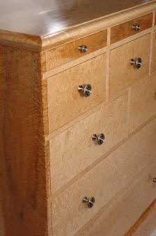 Close-up view of a wooden dresser with six drawers, each featuring round metal knobs, showcasing a light wood grain finish.