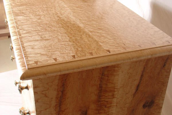 Close-up view of a wooden dresser featuring dovetail joints on the top edge and a polished, light wood grain finish.