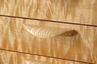 Close-up of a wooden dresser drawer with a curved handle, showing a distinctive wavy wood grain pattern.