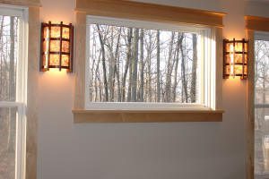 A rectangular window with wooden trim shows a view of leafless trees, flanked by two wall-mounted lights with warm illumination.