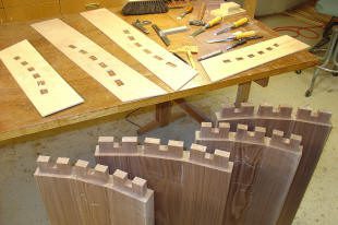 Wooden boards with dovetail joints and chisels are arranged on a workbench in a woodworking shop.