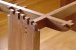A close-up view of wooden beams joined together using a traditional dovetail joint on a hardwood floor.