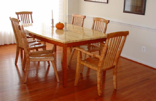 A wooden dining table with six matching chairs, a single candle, and a small pumpkin placed on top, situated in a sunlit room with hardwood floors.