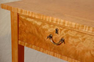 Close-up of a wooden table featuring a single drawer with a metal handle and keyhole, highlighting the wood grain pattern.