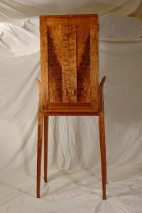 Tall wooden cabinet with two doors and long slender legs, set against a plain white fabric backdrop.