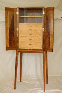 Tall wooden cabinet with two open doors, five drawers, an open shelf at the top, and long legs, displayed against a plain backdrop.