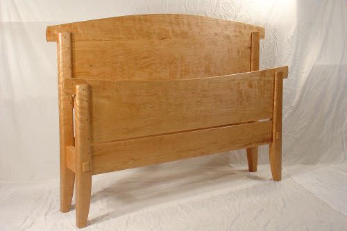 A wooden bed frame with a high, curved headboard and a lower, slightly curved footboard, set against a plain white background.