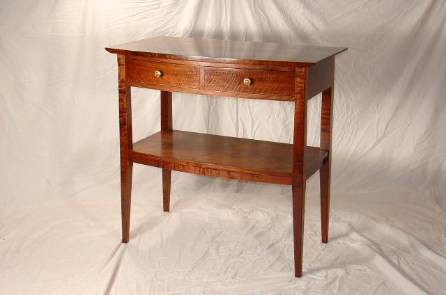 Wooden table with tapered legs, a single drawer with two knobs, and a lower shelf, set against a plain white backdrop.