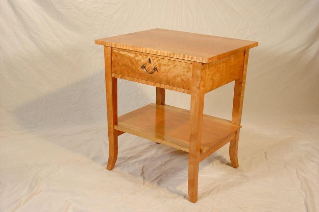 Wooden bedside table with a single drawer, metal handle, and lower shelf, placed on a light fabric backdrop.
