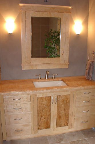 Light wood bathroom vanity with a rectangular sink, a large mirror cabinet above, two wall sconces, and a towel ring with a towel on the right side.