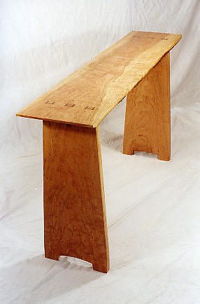 A simple wooden bench with a flat top and two wide, rectangular legs, set against a plain white background.