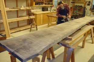 A person in a workshop uses a circular saw to cut a large wooden plank resting on two sawhorses.