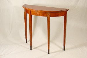 A wooden demilune table with four straight legs and a polished half-moon shaped top, set against a neutral background.