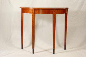 A wooden demilune table with four straight legs, shown against a plain white background.