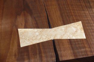 A light wood bowtie inlay reinforces a crack in a darker wood surface.