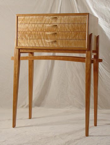 A wooden chest with four drawers sits atop tall, slender legs against a neutral backdrop.