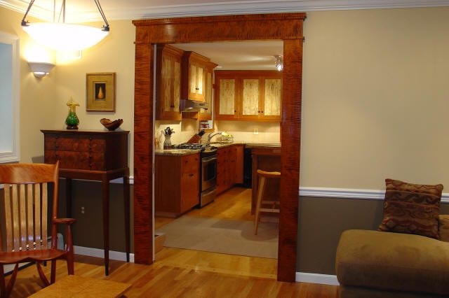 View from a living room into a kitchen with wood cabinetry and stainless steel appliances, separated by a wooden framed doorway.