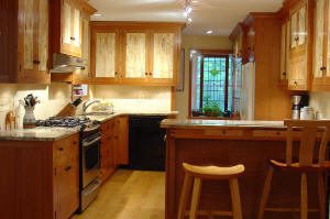 Modern kitchen with wood cabinets, stainless steel appliances, a small breakfast bar with two stools, and a window at the far end letting in natural light.