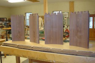 Four wooden panels with dovetail joints are standing upright on a workbench in a woodworking shop.