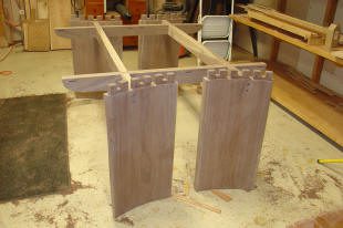 Partially assembled wooden table frame with visible dovetail joints in a workshop setting.