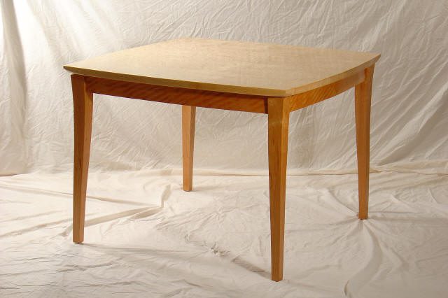 A wooden table with four legs stands on a white fabric backdrop.