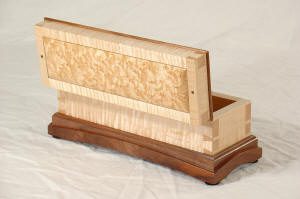 A rectangular wooden box with a hinged lid is open, displaying natural wood grain patterns and a contrasting dark wood base.
