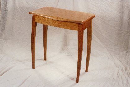 A small wooden table with four slightly curved legs, set against a plain, draped white background.