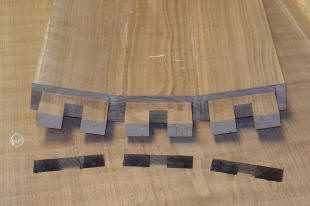 Close-up of a wooden dovetail joint in progress, showing interlocking wood pieces and thin dark spacers on a light wood surface.
