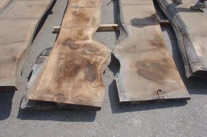 Several large, rough-cut wooden slabs with uneven surfaces and natural edges are laid out on an outdoor surface.