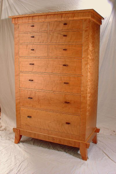 Tall wooden dresser with a smooth, light finish and ten drawers of varying sizes, standing on short, angled legs, placed against a plain fabric backdrop.