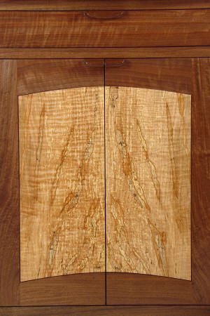 A close-up of wooden cabinet doors with contrasting light and dark wood grain patterns and a drawer above.