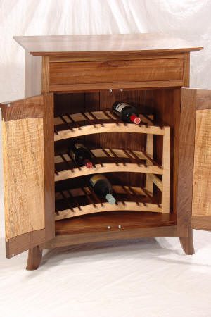 Wooden wine cabinet with open doors showing three shelves, each holding several bottles of wine, and a closed drawer above the shelves.