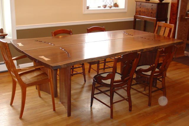 A wooden dining table with a natural edge and six chairs in a dining room with hardwood floors and light-colored walls.